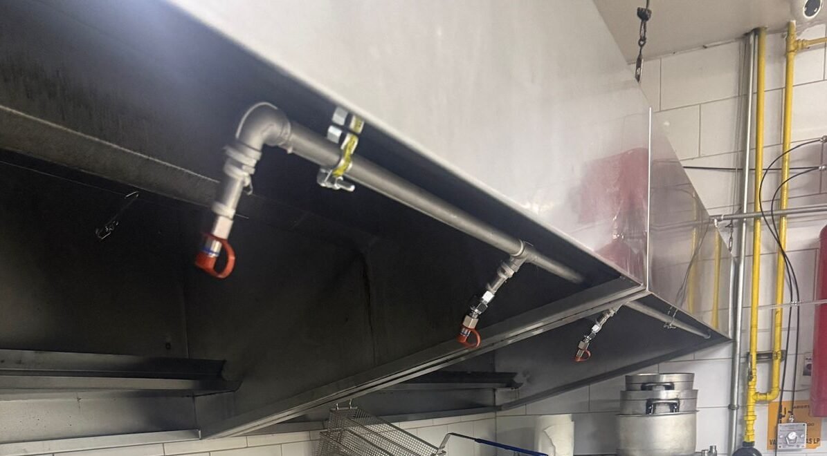 Sistema de supresión para cocina industrial con tubería metálica y boquillas de descarga instaladas bajo campana extractora.